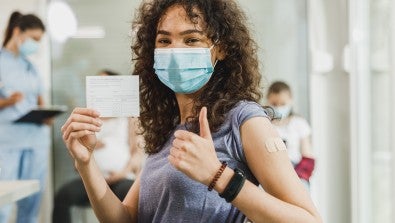 girl with mask on holding up her vaccintion card